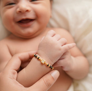 Baby Nazaria black bead gold bracelet worn on newborn wrist Indian evil eye protection charm The Colourful Aura