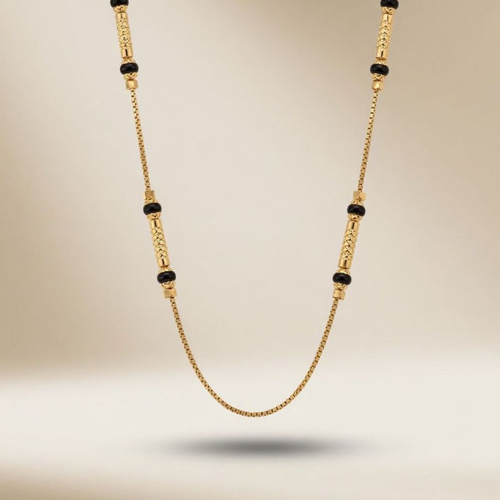 Full length view of a minimalist 18ct gold plated brass chain necklace with black beads on a neutral background