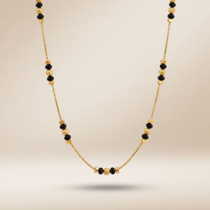 Full length view of an 18ct gold plated necklace with textured gold ball beads and black beads on a neutral background