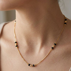 Close-up of a woman wearing an 18ct gold plated black and gold ball bead necklace at the collarbone