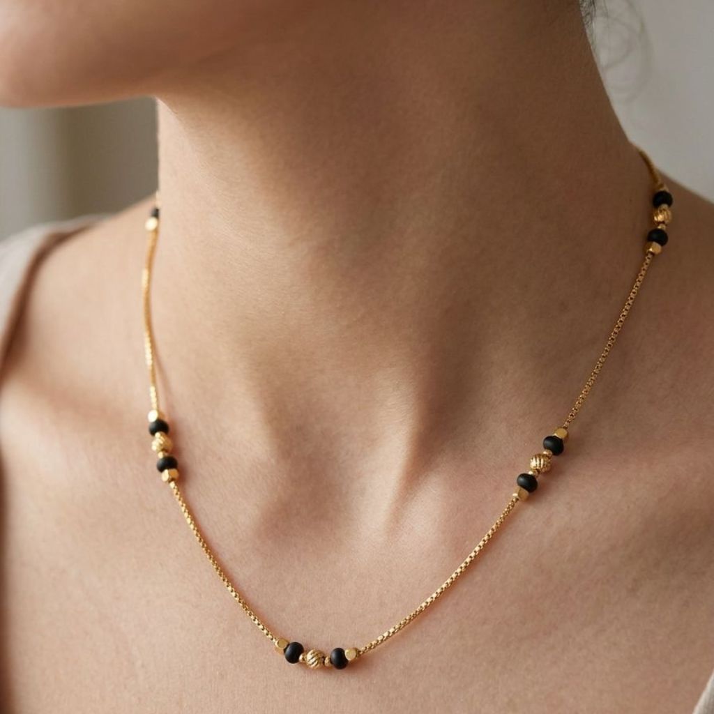 Close-up of a woman wearing an 18ct gold plated black and gold ball bead necklace at the collarbone