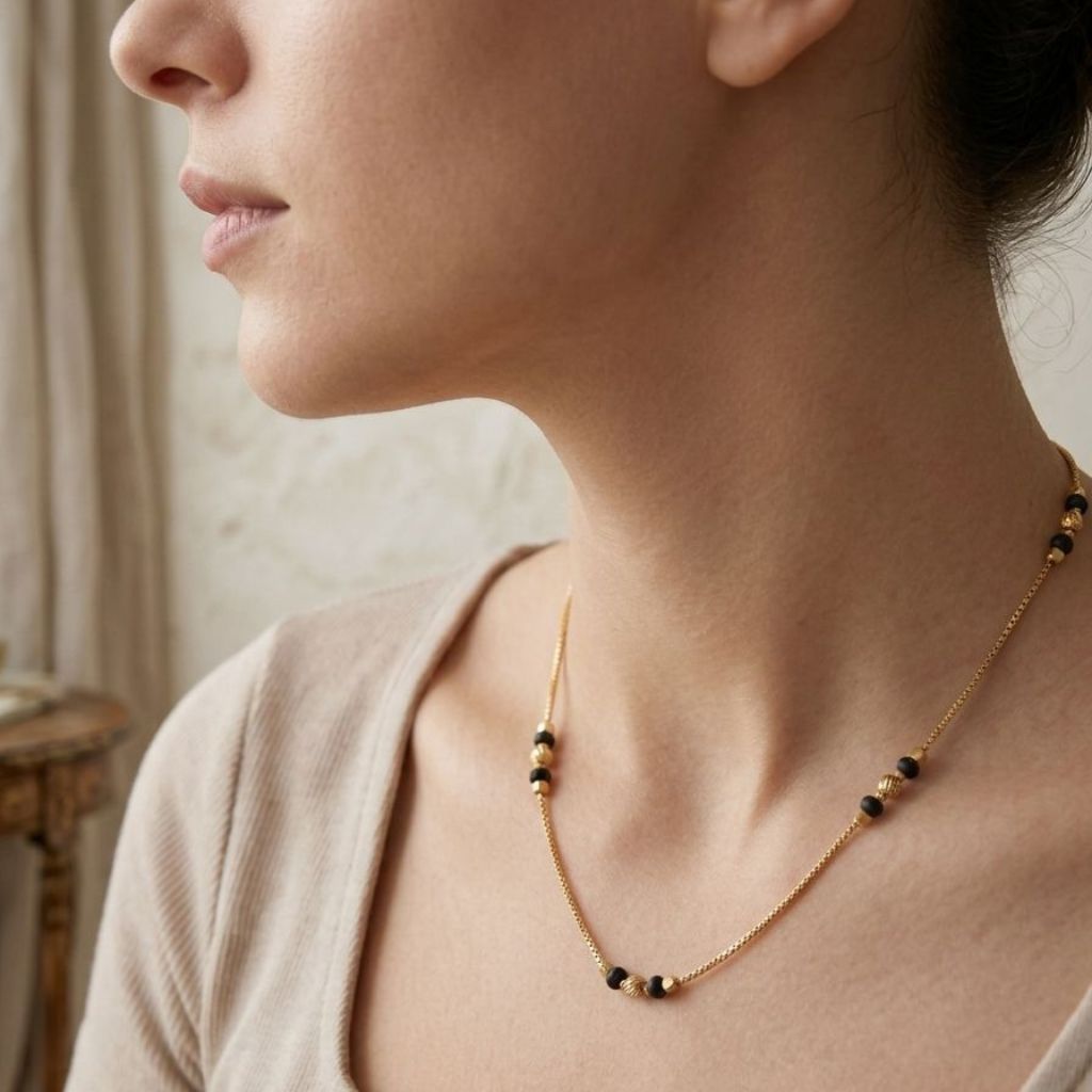 Side profile of a woman wearing a minimalist black and gold ball bead necklace with a nude top