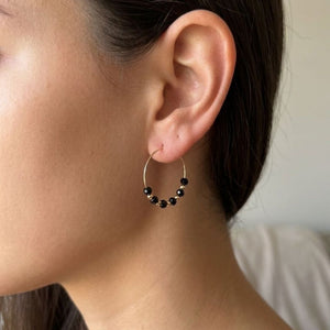 Close-up of a woman wearing black faceted glass bead gold hoop earrings, 30mm gold plated alloy