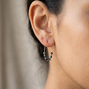 Close-up of a woman wearing navy blue faceted glass bead gold hoop earrings, 30mm gold plated alloy