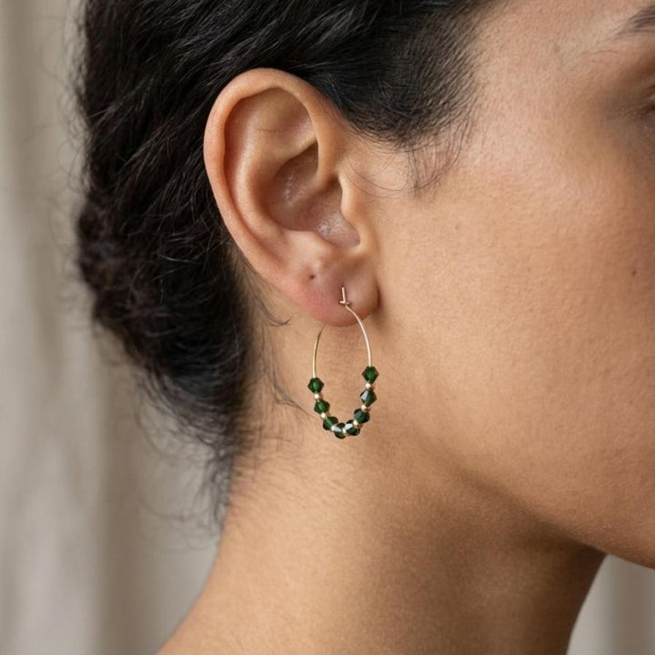 Close-up of a woman wearing emerald green faceted glass bead gold hoop earrings, 30mm gold plated alloy