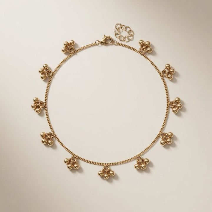 Flat lay of an 18ct gold plated brass bracelet with dangling ball cluster charms and lobster clasp on a neutral background