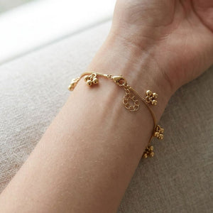 Woman wearing a gold ball cluster charm bracelet at a café table holding a coffee cup, styled with a rust linen top