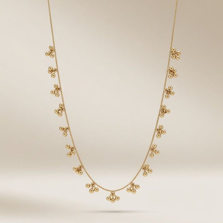 Full length view of an 18ct gold plated brass necklace with dangling ball cluster charms on a neutral background