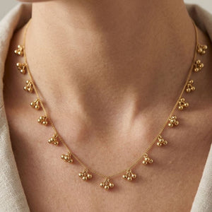 Close-up of a woman wearing an 18ct gold plated ball cluster charm necklace at the collarbone with a linen top