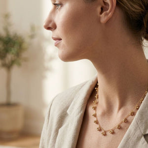 Side profile of a woman wearing a gold ball cluster charm necklace with a linen blazer in a bright interior