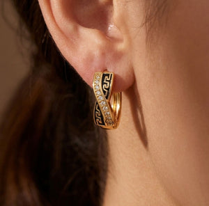 Close-up detail of gold crossover huggie hoop earring showing black Greek key enamel and crystal pavé band