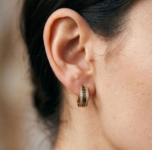 Close-up detail of gold Greek key huggie hoop earring worn on ear showing black enamel and crystal detail