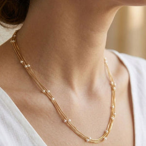 Close up of gold plated triple layer pearl station necklace worn by model in white top