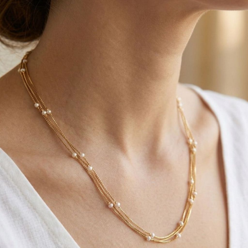 Close up of gold plated triple layer pearl station necklace worn by model in white top