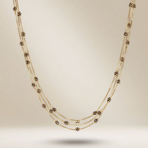 Full length view of an 18ct gold plated triple strand necklace with black and gold spot beads on a neutral background