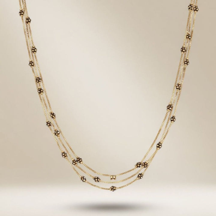 Full length view of an 18ct gold plated triple strand necklace with black and gold spot beads on a neutral background